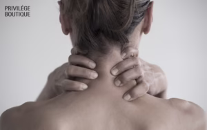 Back view of person with hands clasped around neck, highlighting skin contours in soft lighting with boutique branding.