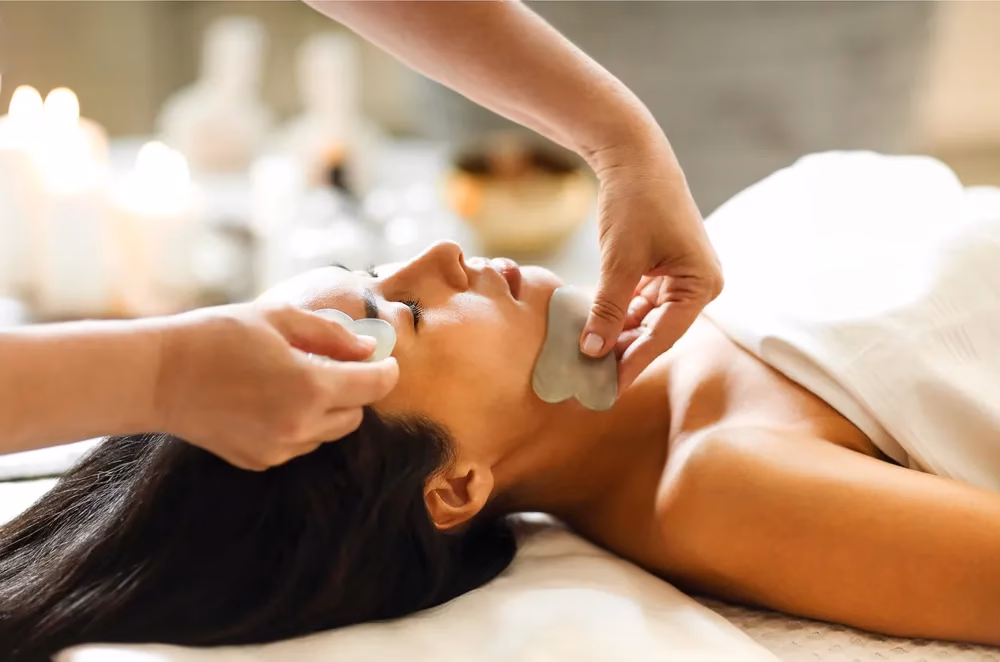 A woman receiving a Gua Sha facial treatment at a spa.